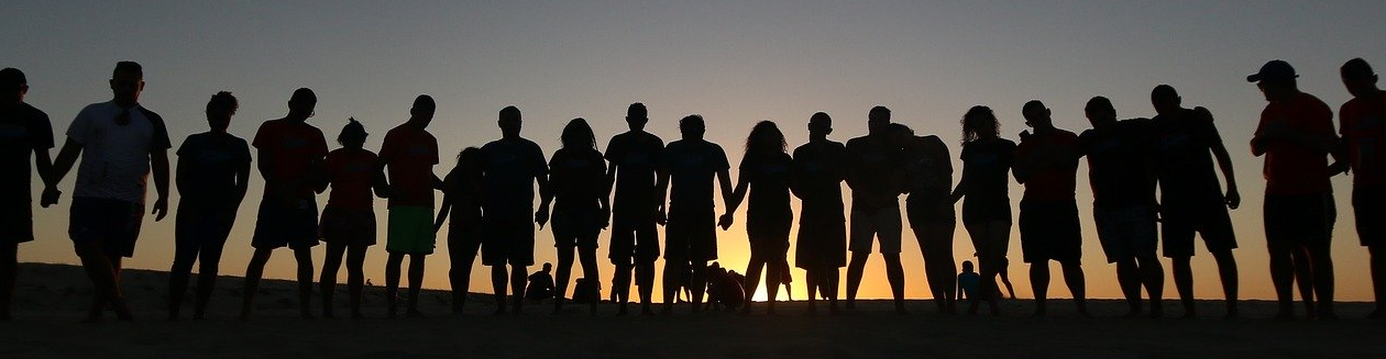 Group of people with linked hands silhouetted by sunset. 