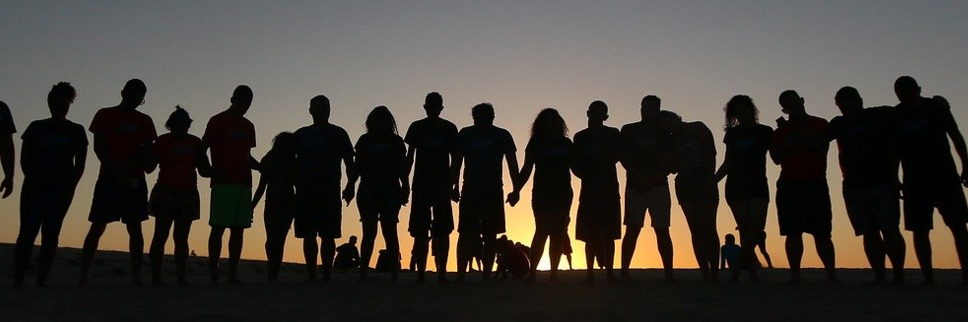 Group of people with linked hands silhouetted by sunset. 