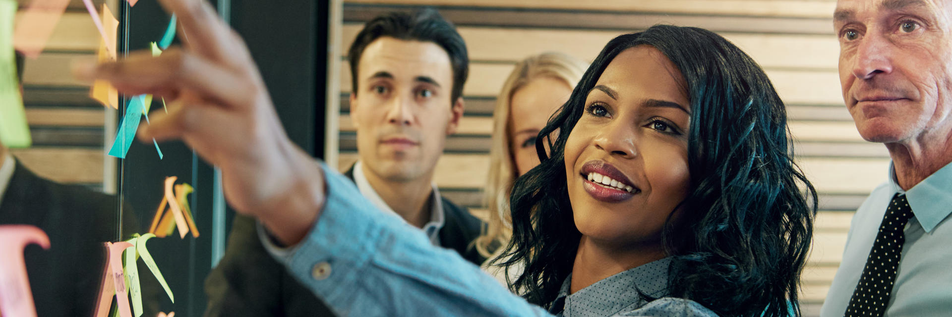 Woman pointing to notes on board; coworkers look on. 